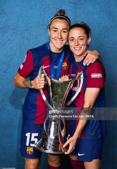 two female soccer players hugging each other with the trophy in front of blue wall stock photo