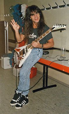 a man with long hair sitting on top of a bench holding an electric guitar in his hand