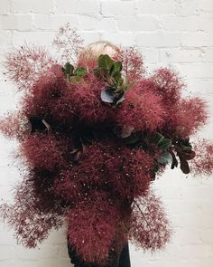 a vase filled with lots of red flowers on top of a wooden table next to a white brick wall