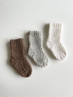 three knitted socks sitting next to each other on a white surface, one is brown and the other is beige