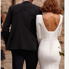 a man and woman dressed in formal wear walking down the street with their back to each other