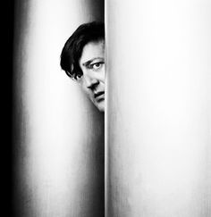 black and white photograph of a person peeking out from behind two tall poles with their head between them