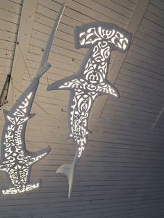 two metal sculptures hanging from the side of a white building with intricate designs on it