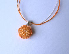 an orange slice is attached to a cord on a white surface with a silver clasp