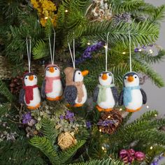 small penguin ornaments hanging from a christmas tree with pine cones and purple flowers in the background