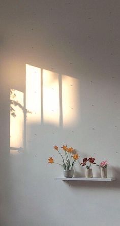 three white vases with flowers are on a shelf in the corner of a room