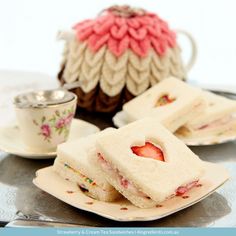 small sandwiches with strawberries in the middle on a plate next to a teapot