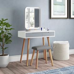 a white dressing table with a mirror and stool next to a small potted plant