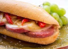 a sandwich with meat, cheese and vegetables on a green plate next to some grapes