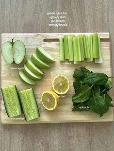 a cutting board topped with sliced up green apples and cucumbers next to slices of lemon