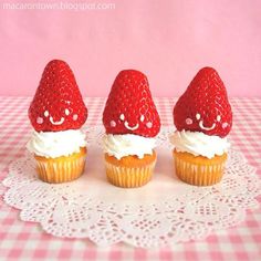 three cupcakes with strawberries are sitting on a doily