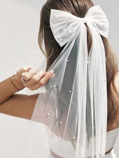 a woman wearing a white veil with a bow on it's head and holding her hair in one hand