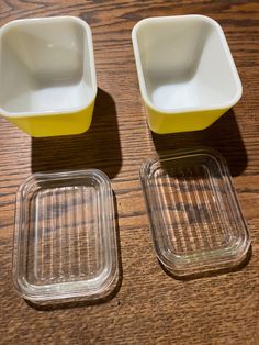 two glass dishes sitting on top of a wooden table next to a yellow cup and saucer