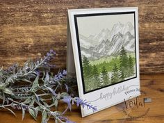 a greeting card with an image of mountains and trees on it, surrounded by greenery