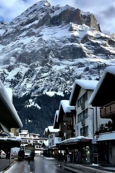 a snowy mountain is in the distance with buildings on both sides and people walking down the street