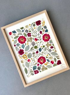 an art work with flowers and leaves in a wooden frame on a gray surface,