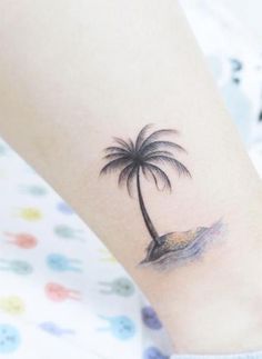 a small palm tree tattoo on the left inner forearm and foot, with an ocean wave coming out of it