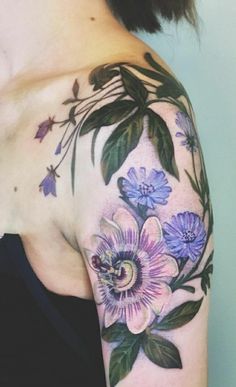 a woman's shoulder with flowers and leaves on her left arm, which is covered in tattoos