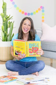 a woman is sitting on the floor and reading a book while smiling at the camera