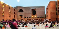 a large group of people sitting around tables in front of a building with lights on