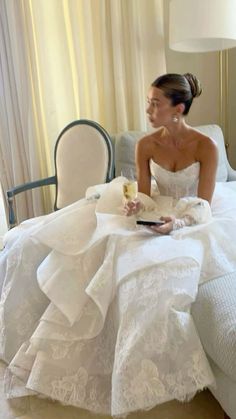 a woman in a wedding dress sitting on a bed with a glass of wine and a book