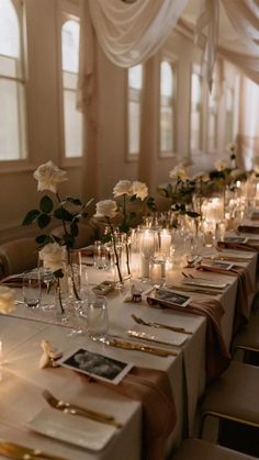 a long table is set with candles and flowers in glass vases, along with place settings