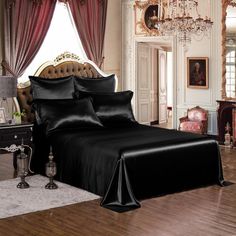 a bed with black sheets and pillows in a room next to a chandelier