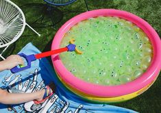 a child playing with an inflatable pool on the grass next to a chair