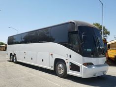 a large white bus parked in a parking lot next to another yellow bus behind it