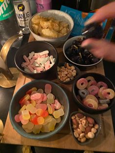 bowls filled with different types of snacks on top of a wooden table next to cans of soda