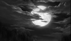 a black and white photo of a full moon in the night sky with dark clouds