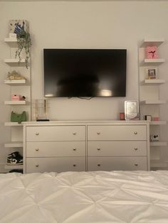 a flat screen tv mounted on the wall above a dresser in a room with white walls