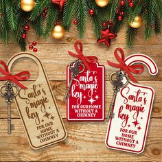 three christmas tags hanging from a tree with red ribbon and ornaments around them on a wooden surface