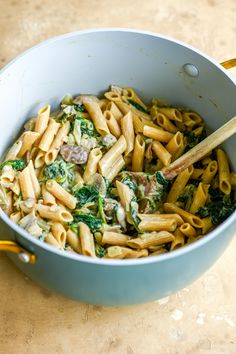 a pot filled with pasta and spinach on top of a wooden table next to chopsticks