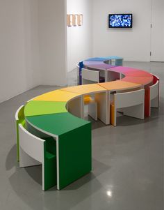 an art gallery with multiple colored tables in the center and a flat screen tv on the wall