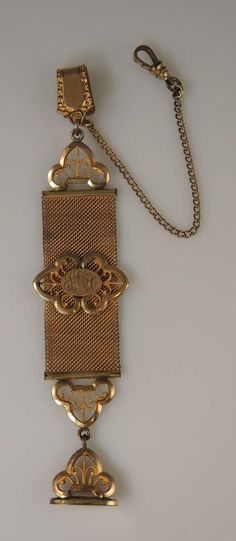 This is a gilt metal Chatelaine which has a hinged, sprung clasp at one end with a spike to secure it securely.  There is also a length of fine mesh links and a dog clip to attach to the watch in the pocket.  The remaining chatelaine would then hang from the pocket. The chatelaine is made up of a strap of fine mesh links with an oval panel with initials SMH. Hanging from it is a matching seal with an oval base and a finely carved handle. The chain measures 140mm from end to end inc the seal, is Fine Mesh, Dog Clip, Chatelaine, Chains Necklace, Favorite Jewelry, A Dog, Initials, Accessory Gift, Jewelry Necklaces