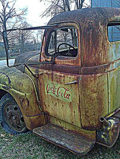 an old rusty coca cola truck sitting in the grass