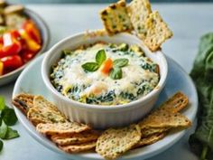 a bowl of spinach dip surrounded by crackers and vegetables