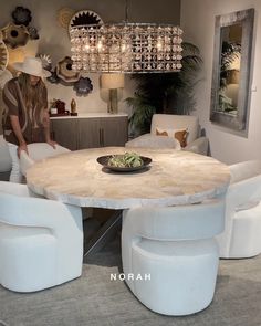 a woman sitting at a round table surrounded by white chairs and chandelier hanging from the ceiling