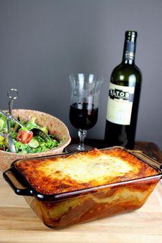 a casserole dish on a table next to a bottle of wine and salad