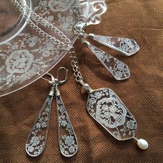 four silver spoons are sitting on top of a glass plate with pearls hanging from it