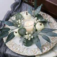 a white plate topped with a candle and some greenery next to a brown suitcase