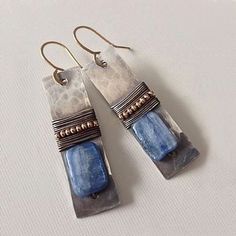 two blue and silver earrings on top of a white surface with beaded wire hanging from them