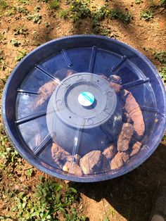 a blue plastic bowl filled with rocks on the side of a dirt road next to grass