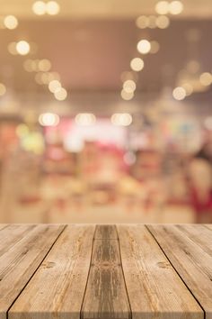 an empty wooden table in front of a blurry storefront with lights on the ceiling