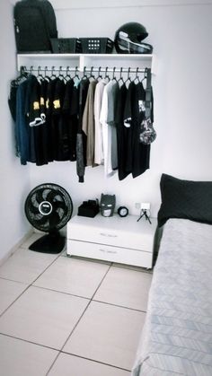 a white closet with clothes hanging on the wall and a bed in the corner next to it