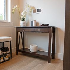 a wooden table sitting in front of a window next to a white vase filled with flowers