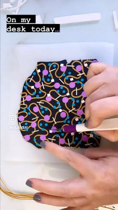 a woman holding onto a black and purple purse with colorful designs on it, next to her nails