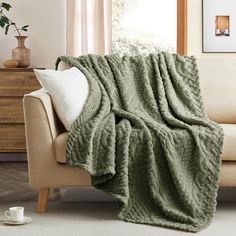 a couch with a blanket on top of it next to a coffee cup and vase