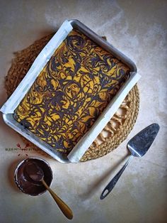 a cake with chocolate frosting in a pan next to spoons on a table